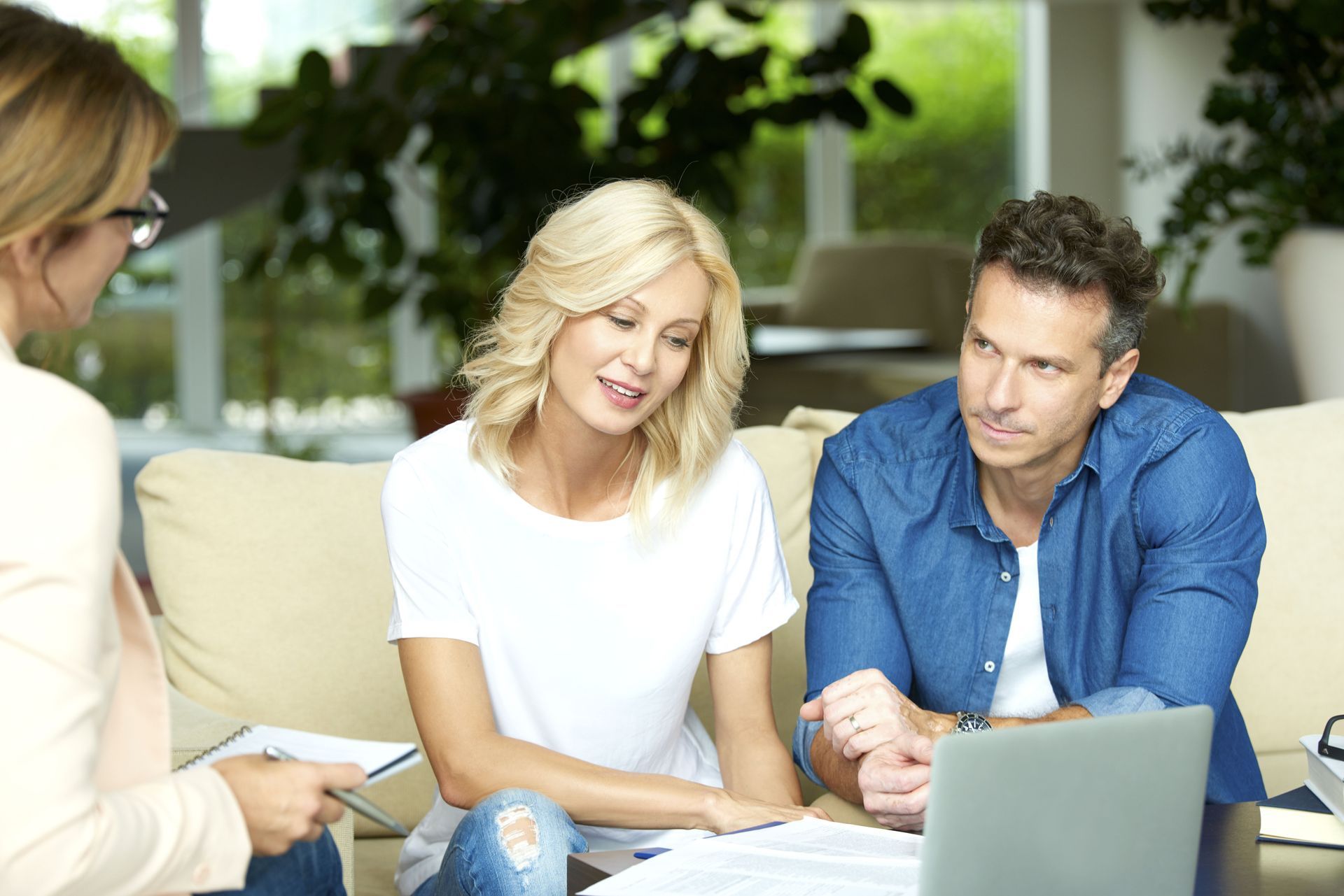 Three people in a meeting, looking at a laptop and papers in a bright office