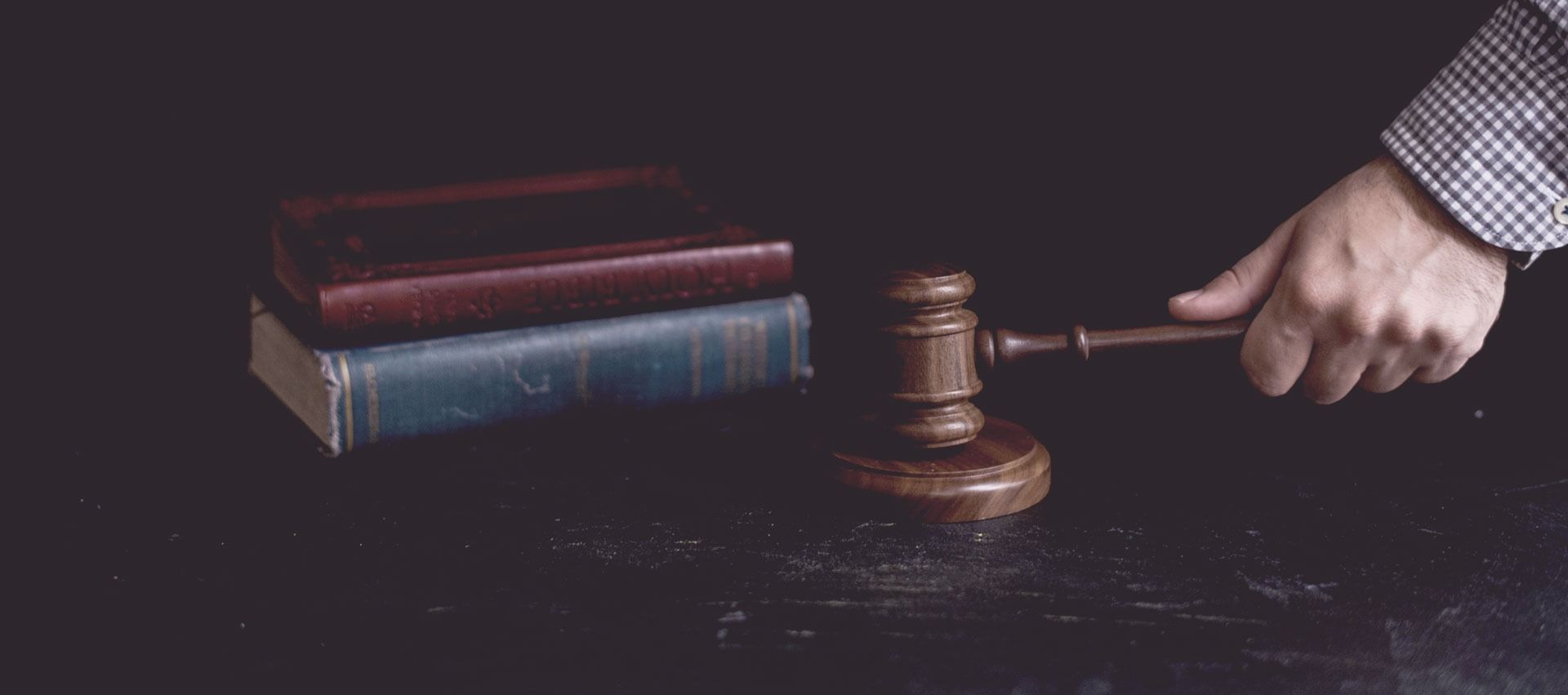 Judge’s gavel beside stacked books on a dark surface, with a hand holding the handle
