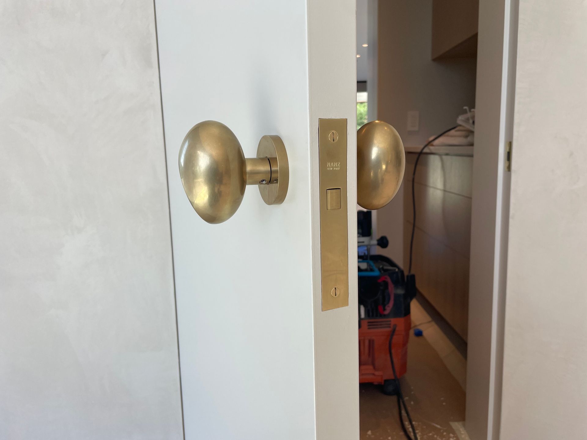 Brass door handle and lock on a partially open white door, revealing a kitchen beyond.