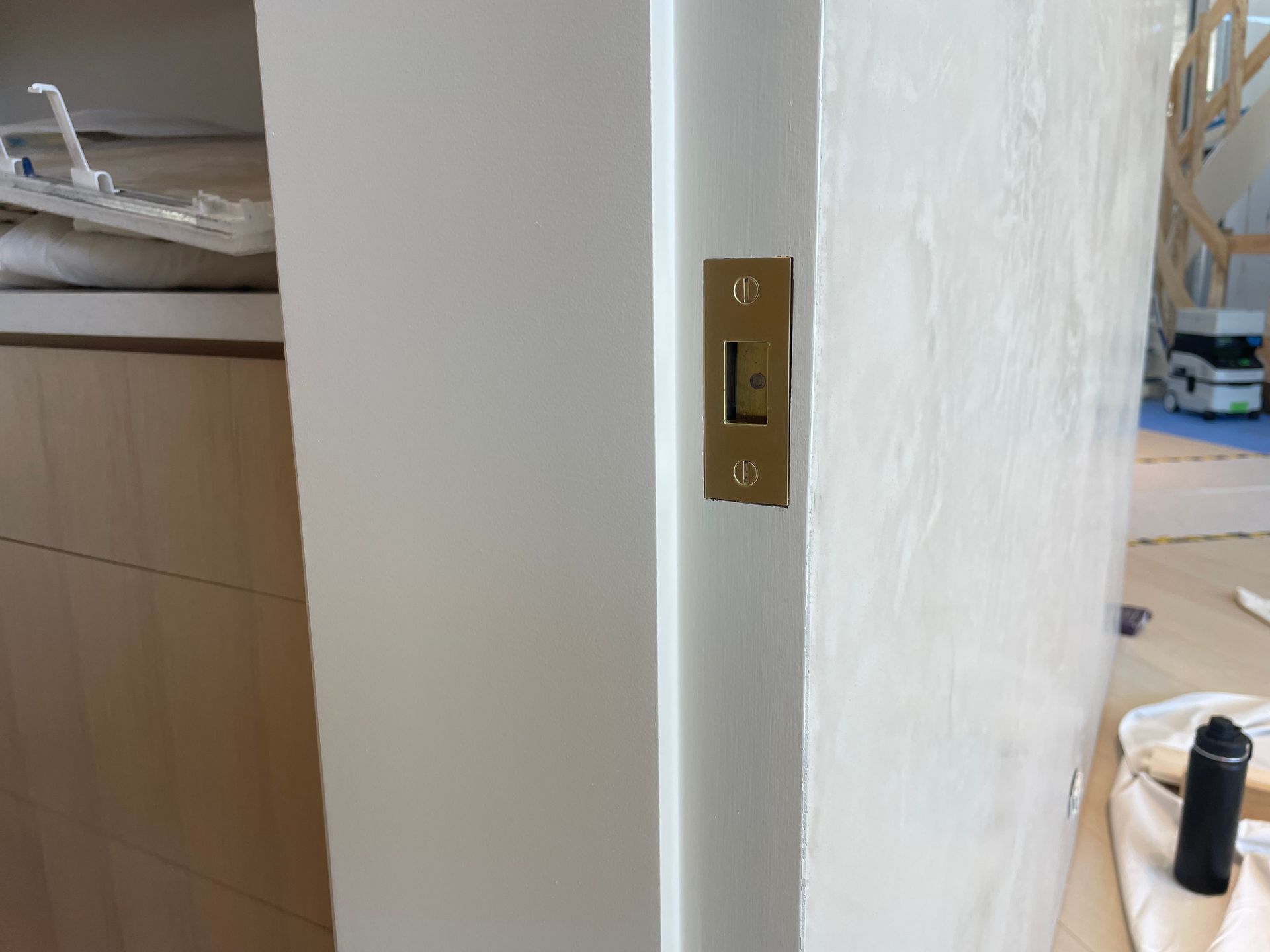 Partially open white door with brass handle, showing a room interior and wooden cabinets beyond.