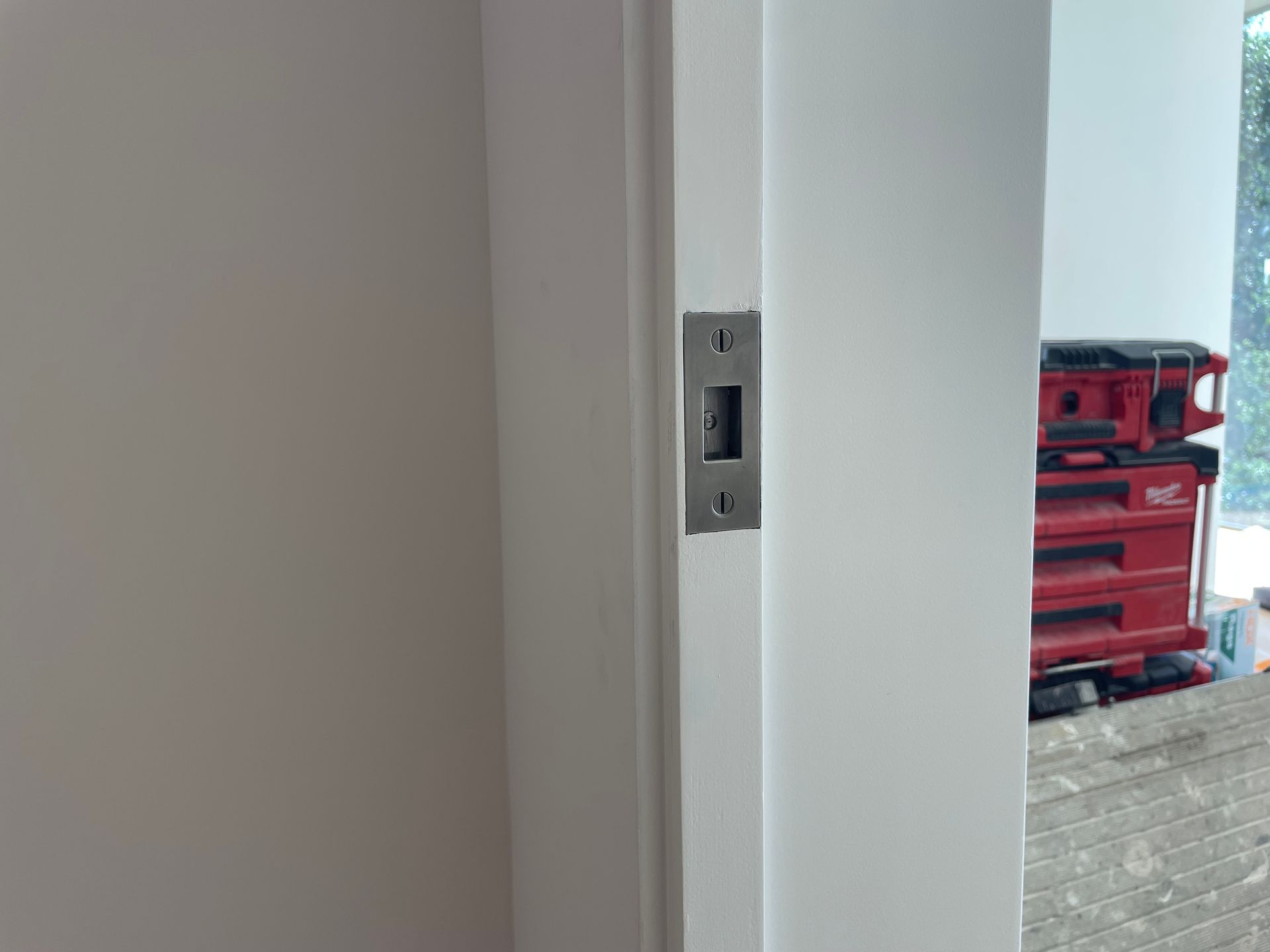 Close-up of a white wall edge with a metal door latch, opening to a red tool chest outside.