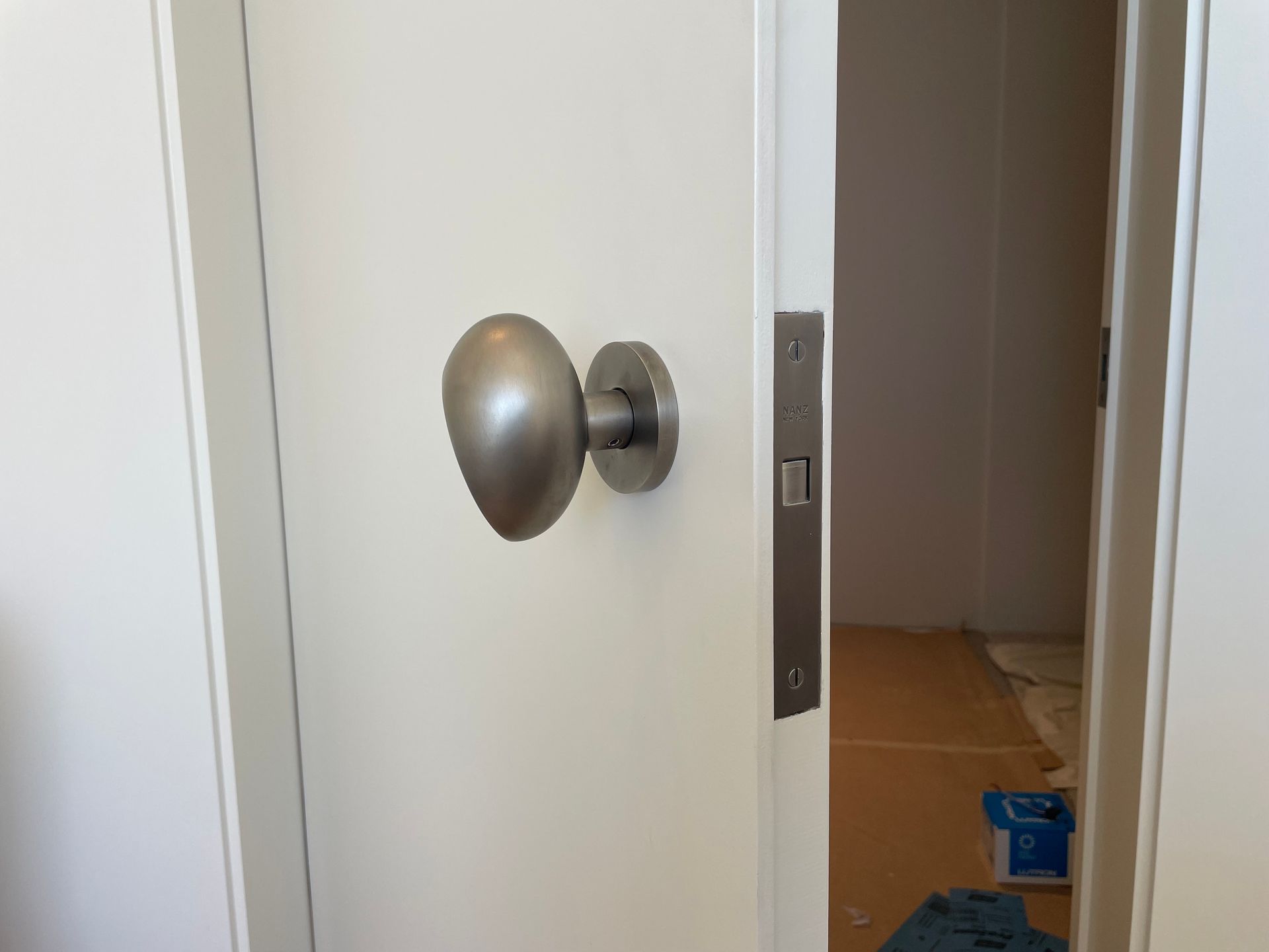 Partially open white door with a silver knob, showing a dim room and floor inside