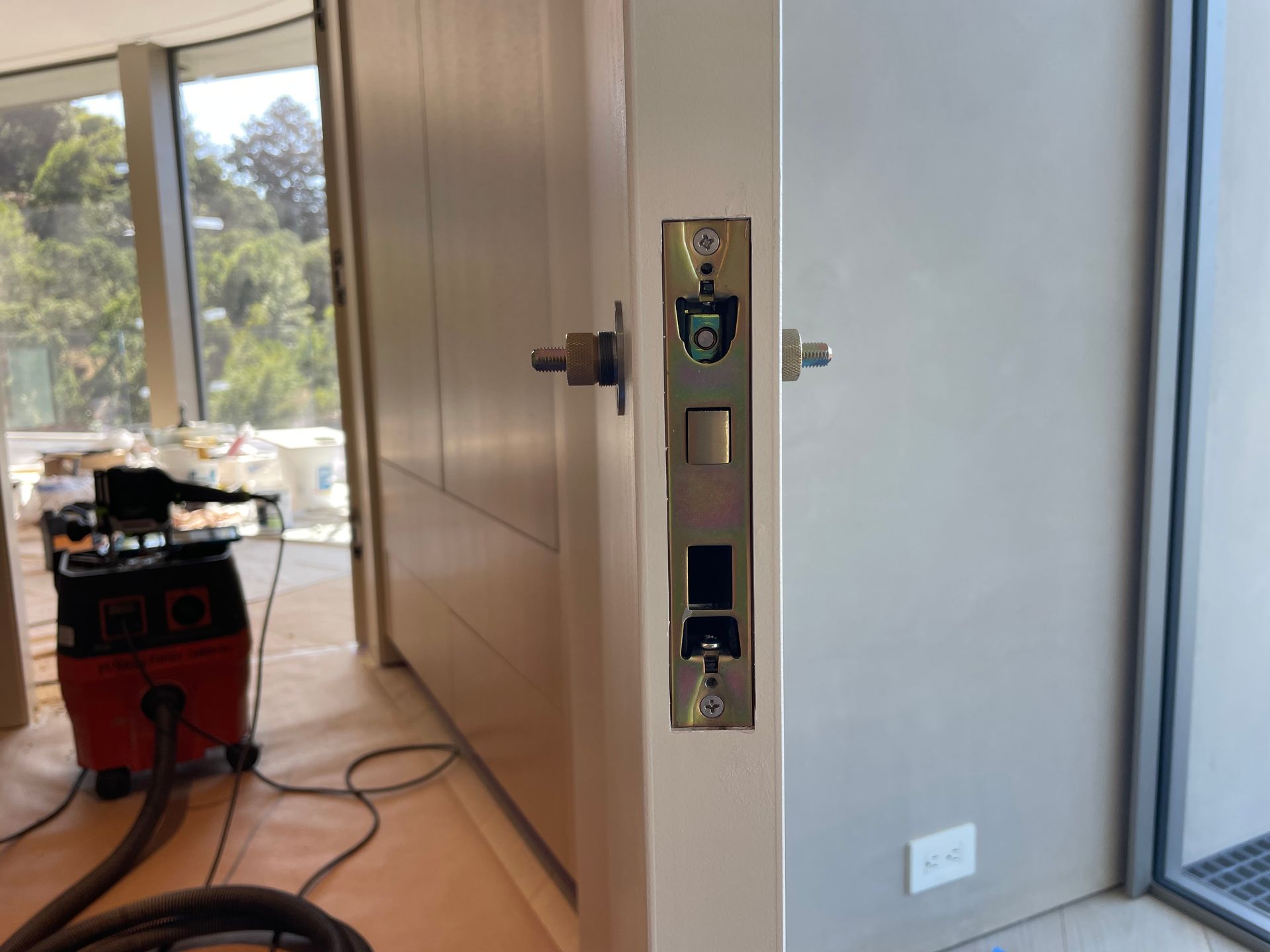 Partially open door with brass lock hardware in a bright room near a window and floor-level outlet