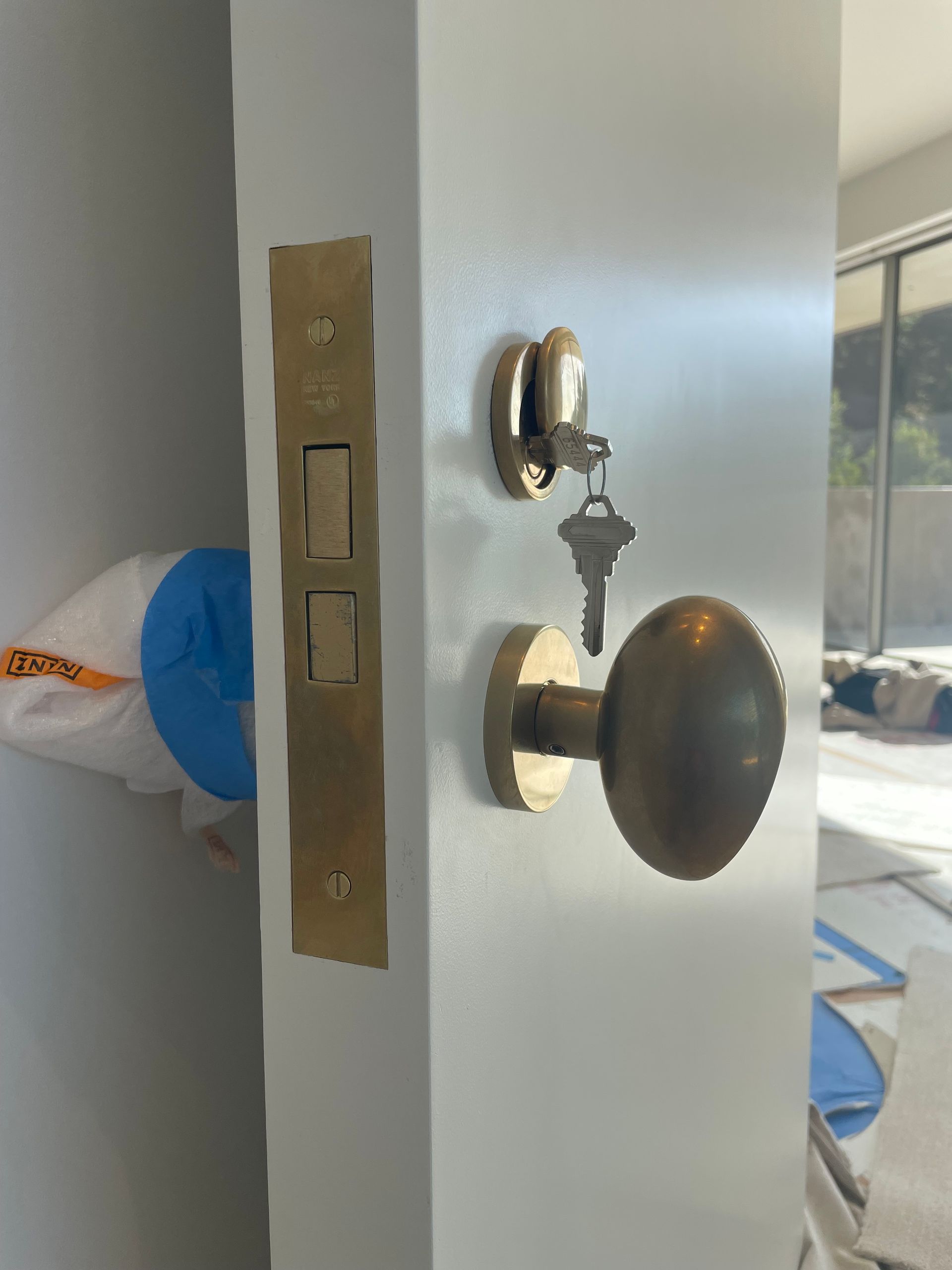 Close-up of a front door with brass lockset and deadbolt, partially open into a bright room.