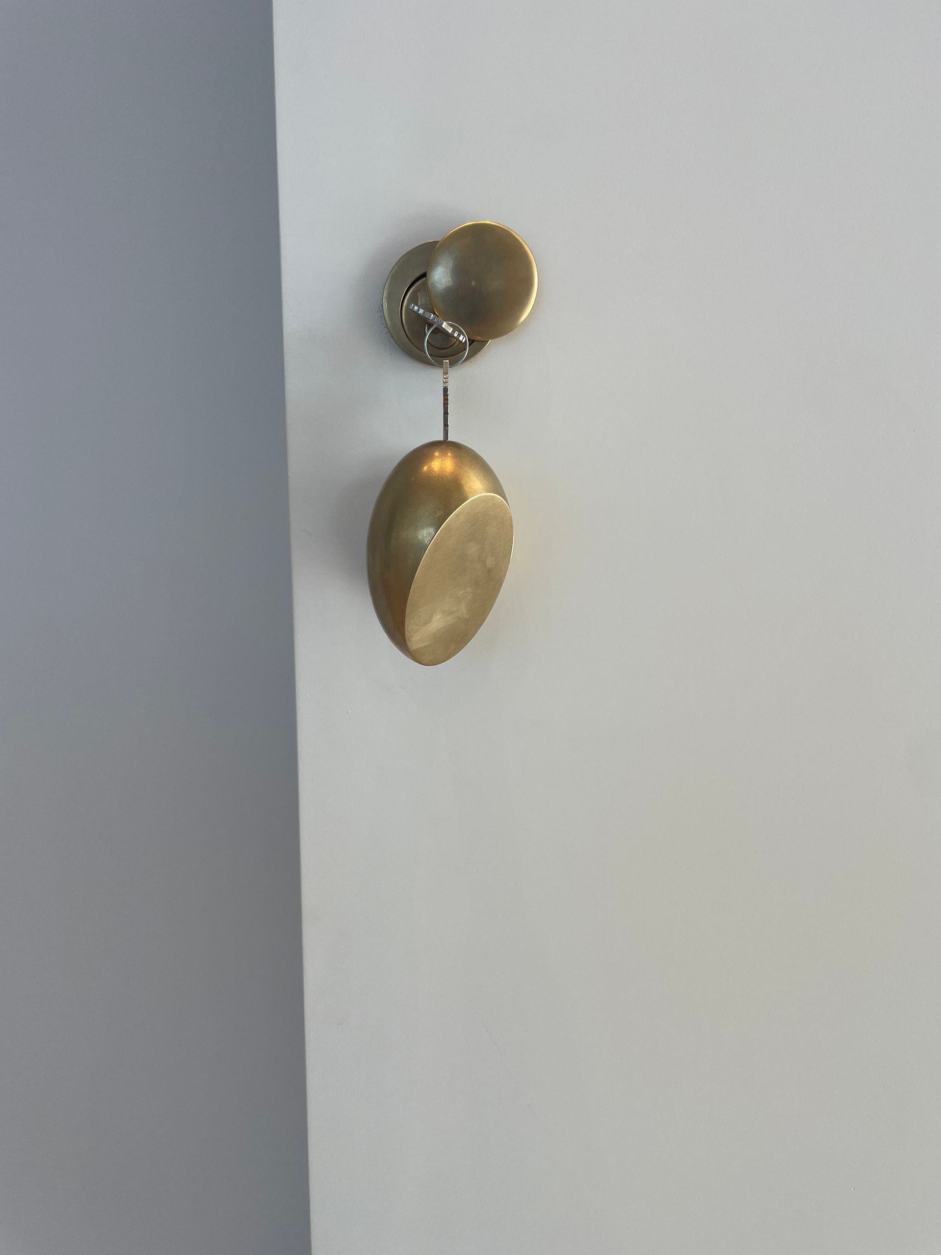 Gold wall hanging with two dangling circular pieces on a light gray wall