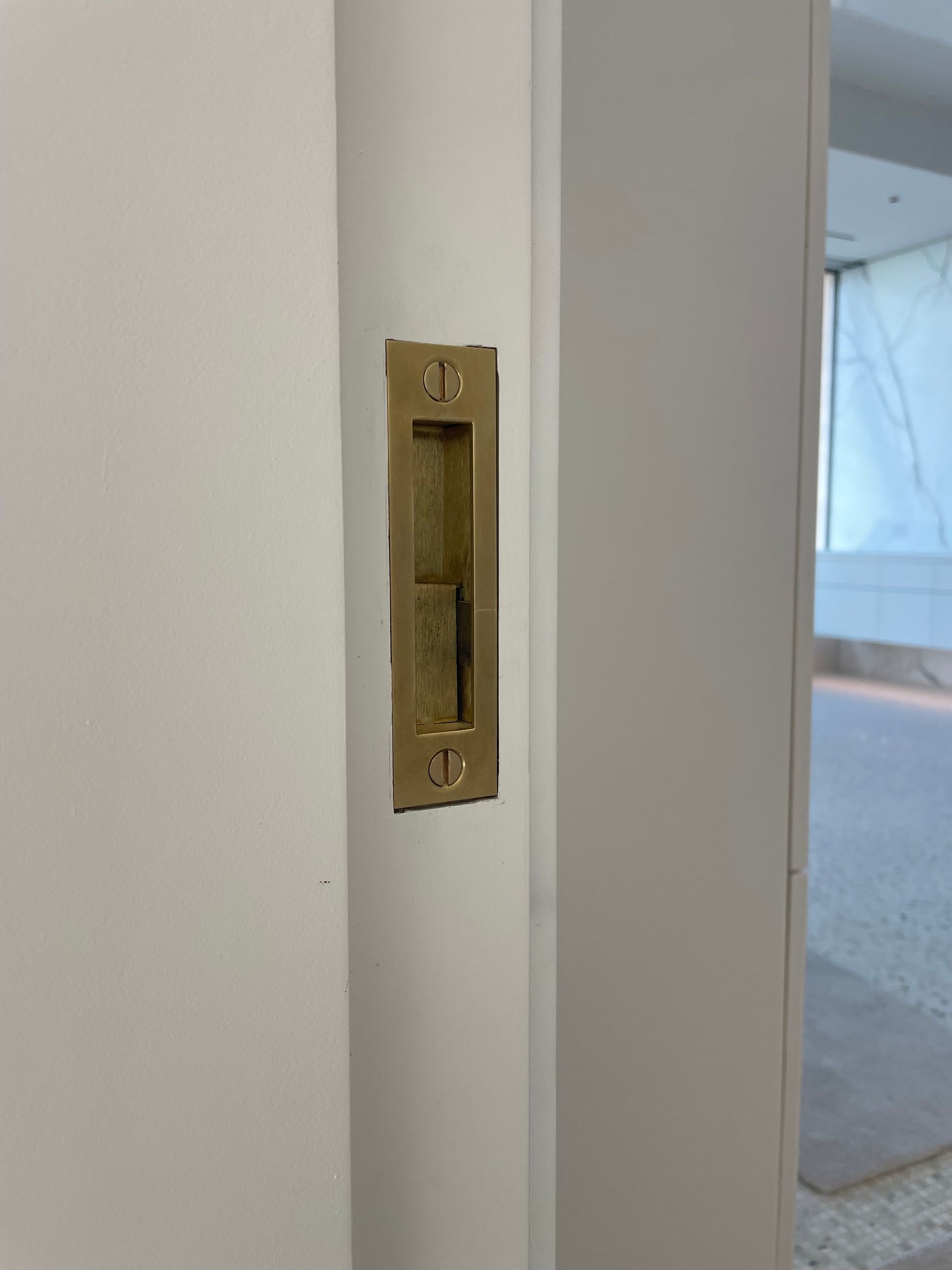 Brass recessed door latch on a white door frame beside an open doorway to a carpeted room