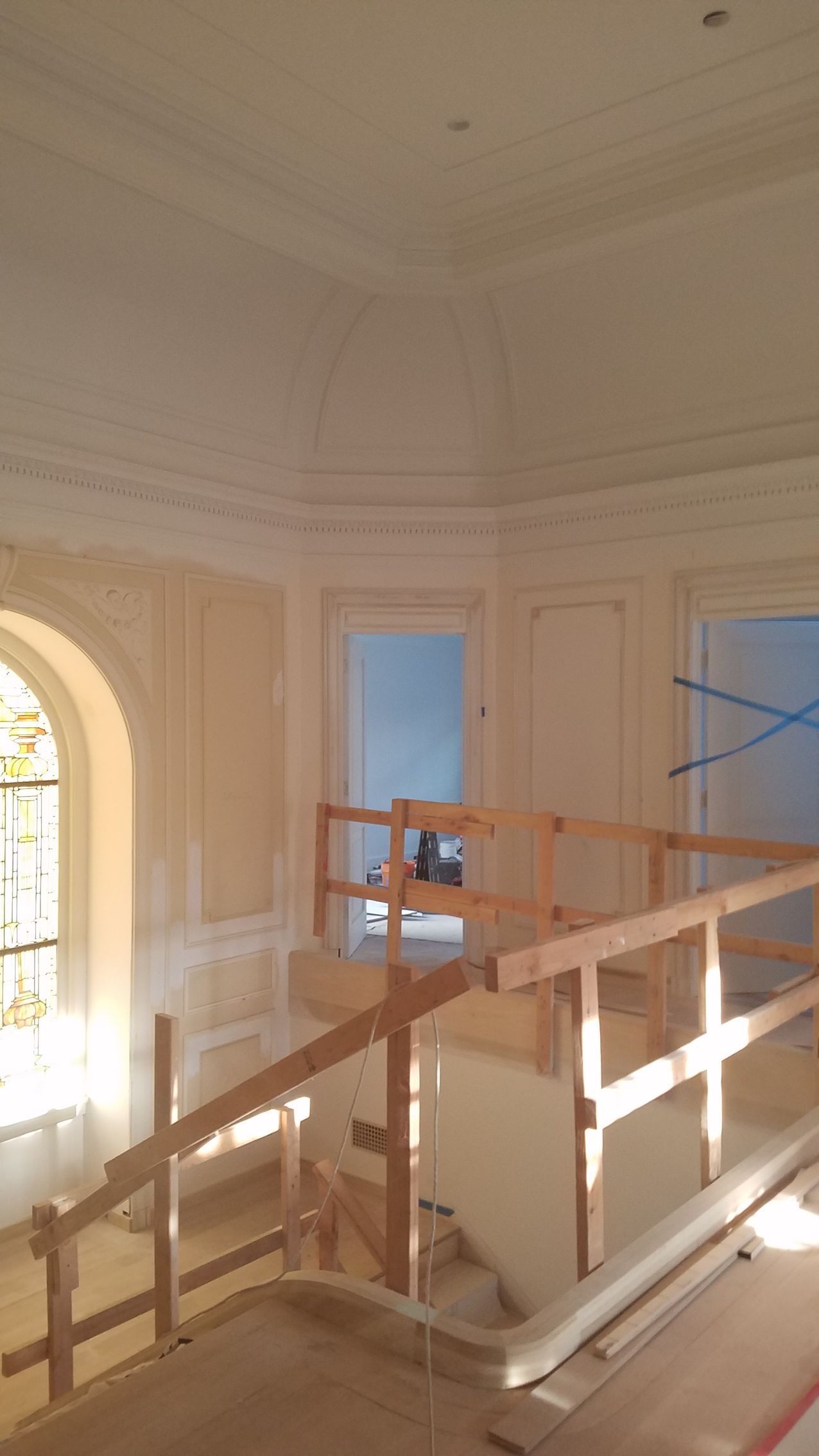 Interior of a building with a staircase under construction, featuring wooden railings and ornate plasterwork.
