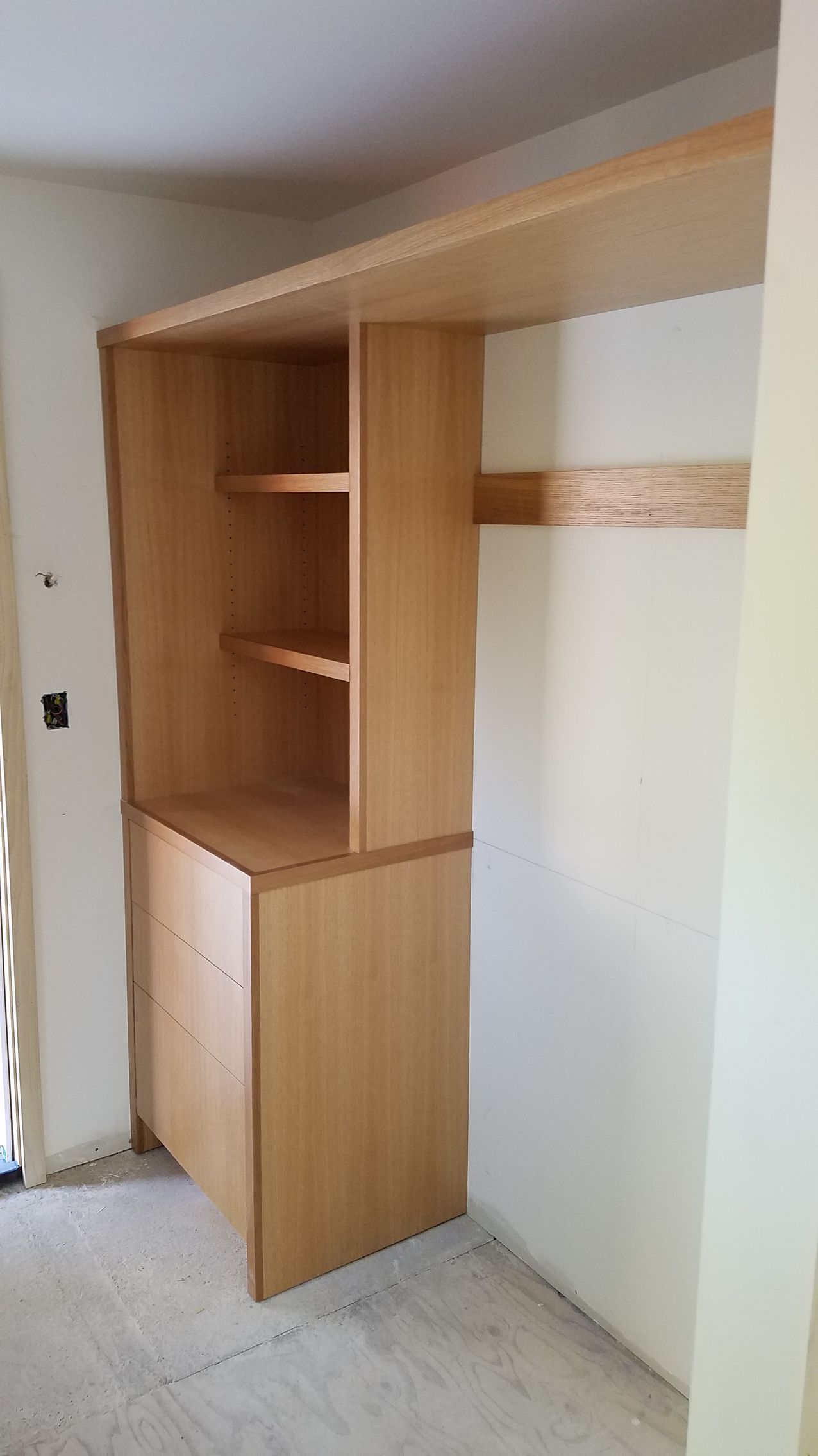 Built-in wooden closet with shelves, drawers, and hanging rod against white walls.