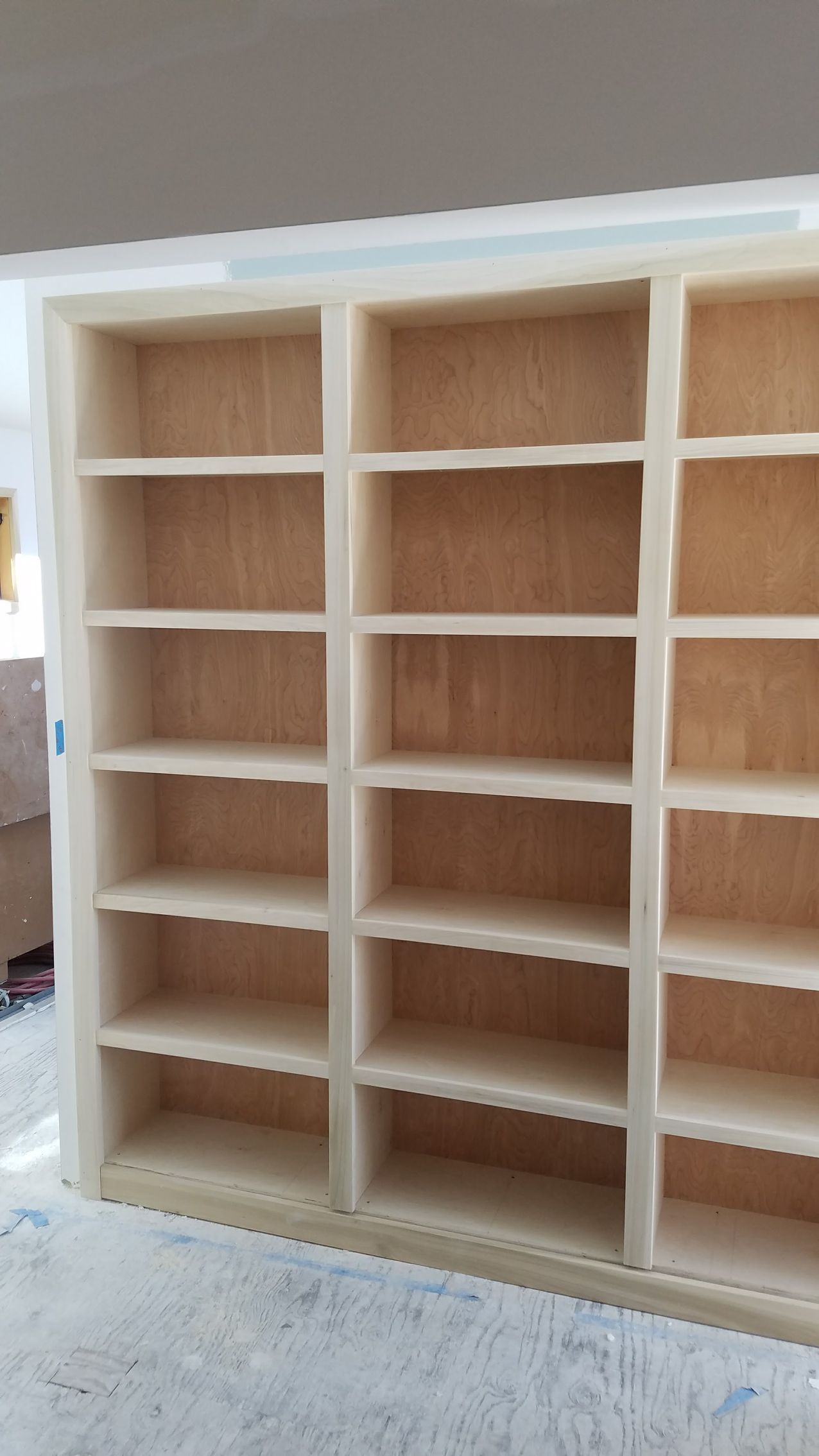 Empty, light-wood bookshelf with three columns of shelves against a wall.