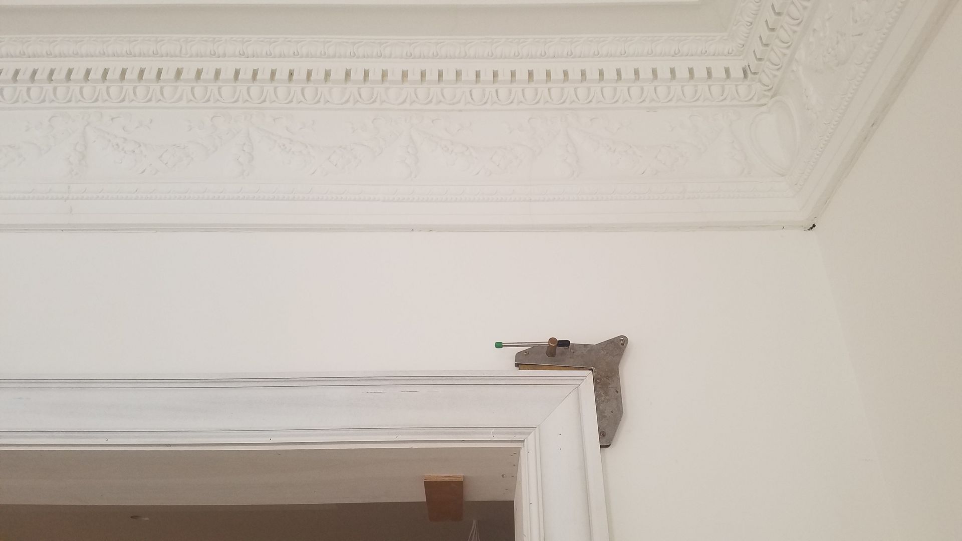 Corner of a white doorway with decorative molding and ornate ceiling trim.