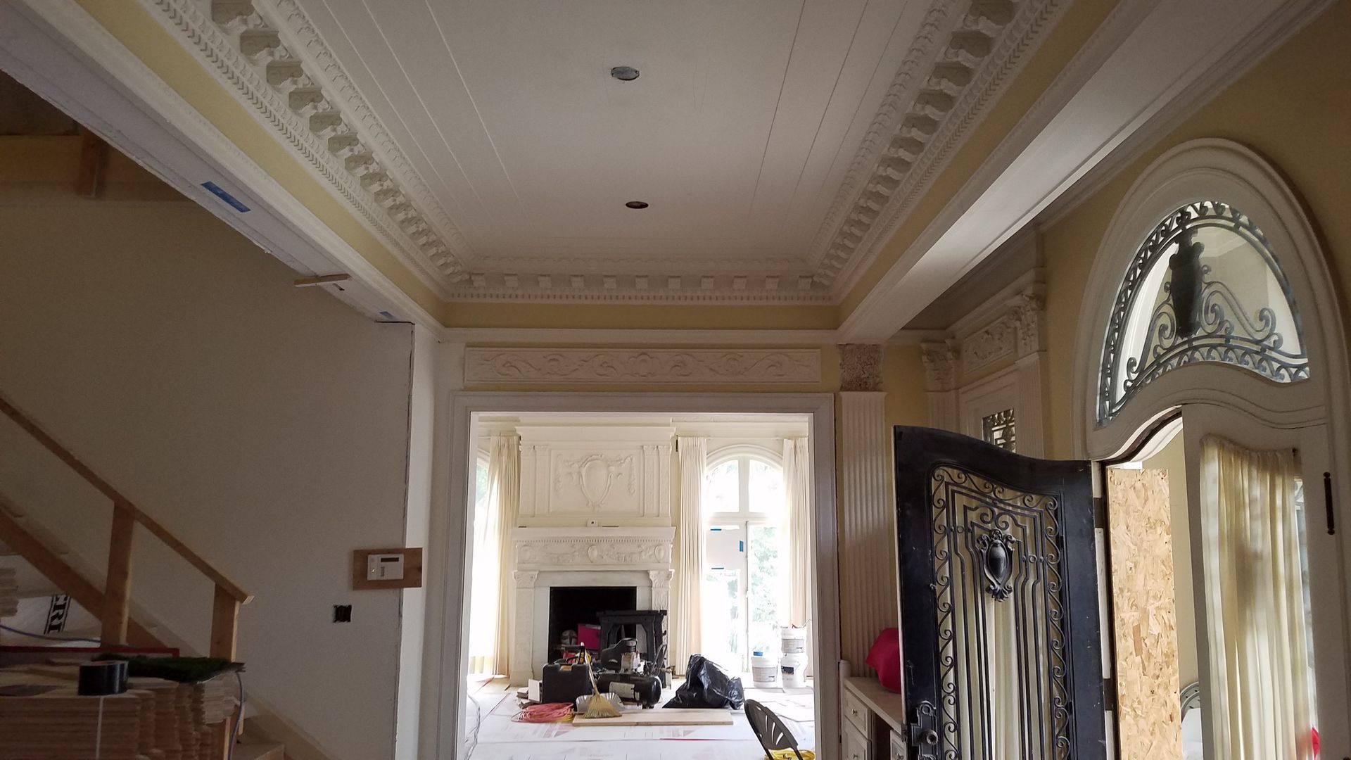 Interior hallway with ornate ceiling molding, doorway to a room with a fireplace, and a partially open front door.