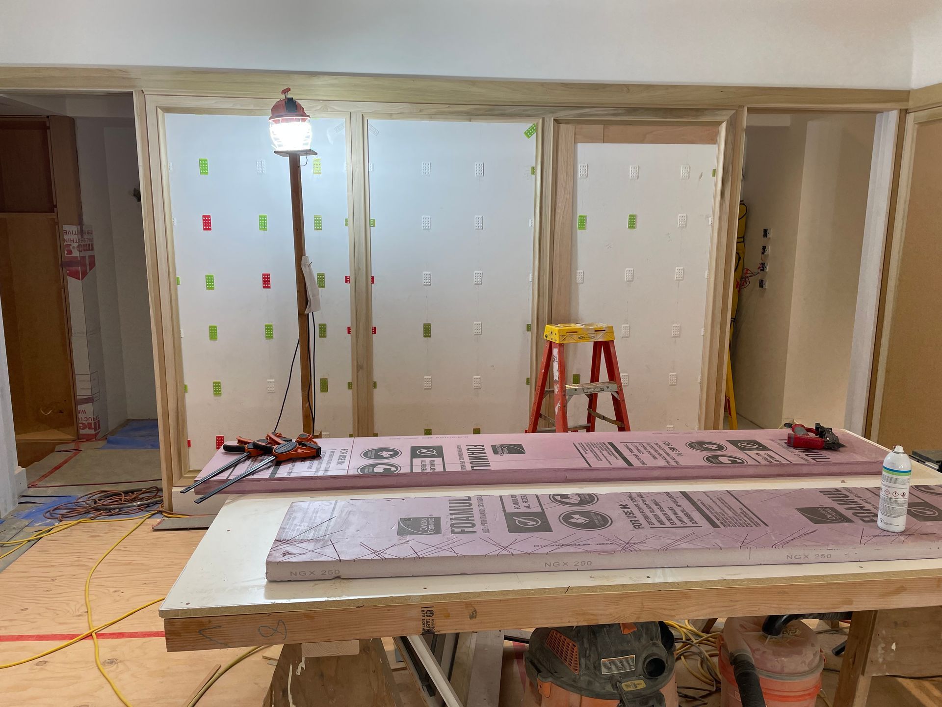 Construction site: Insulation boards on a work table, framed walls with foam insulation attached.