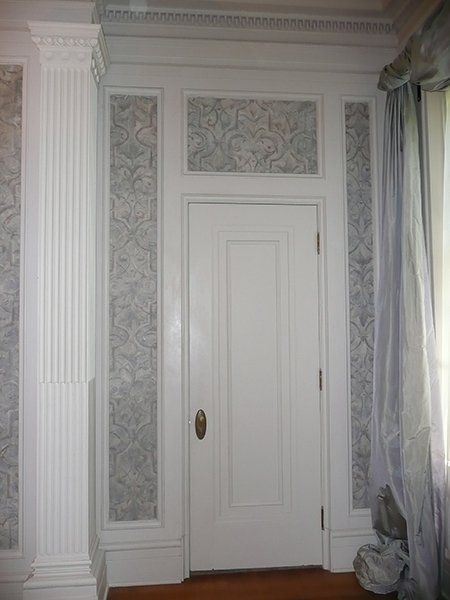 A white door in a room with columns and wallpaper
