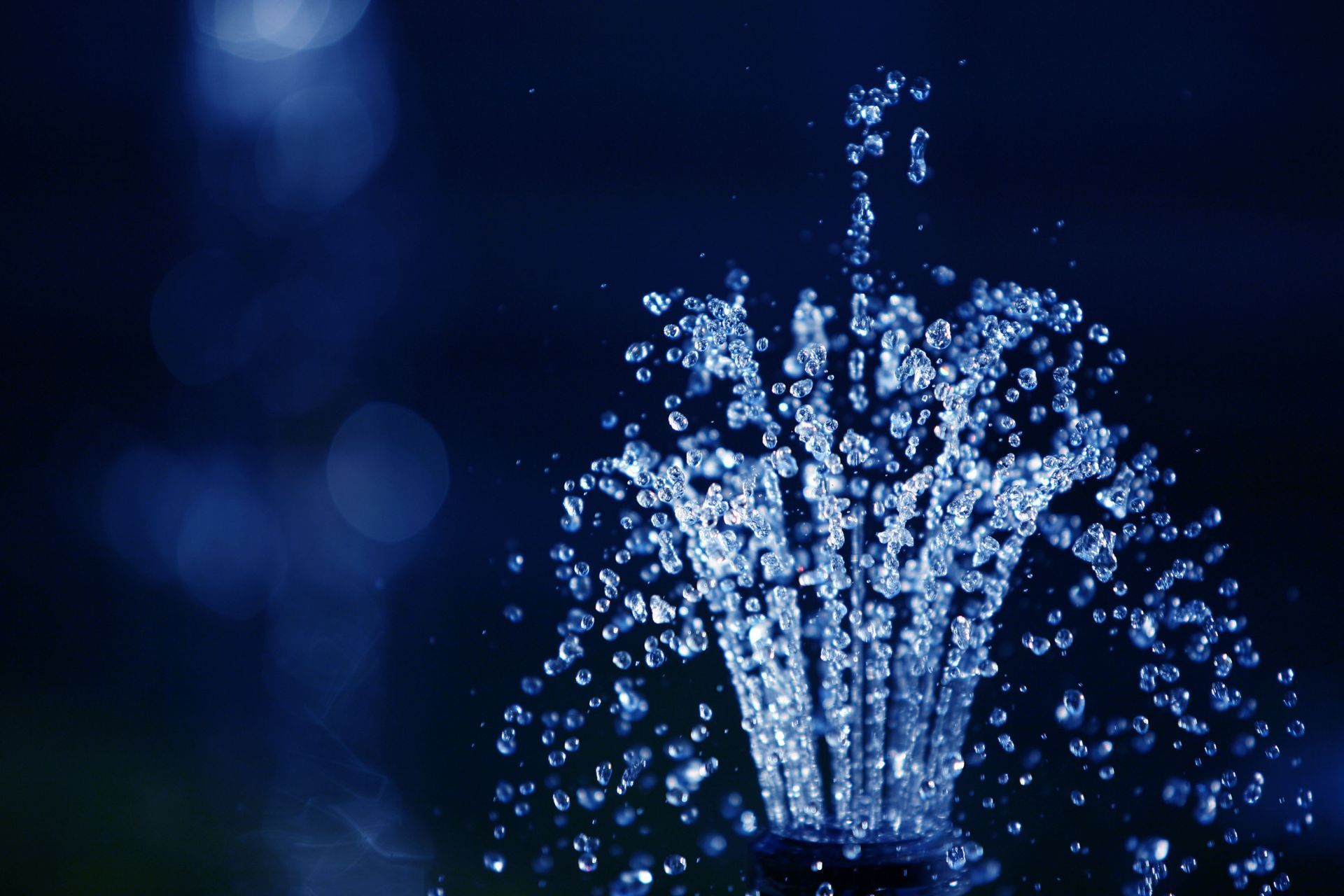 A close-up of a fountain spraying water against a dark blue background.