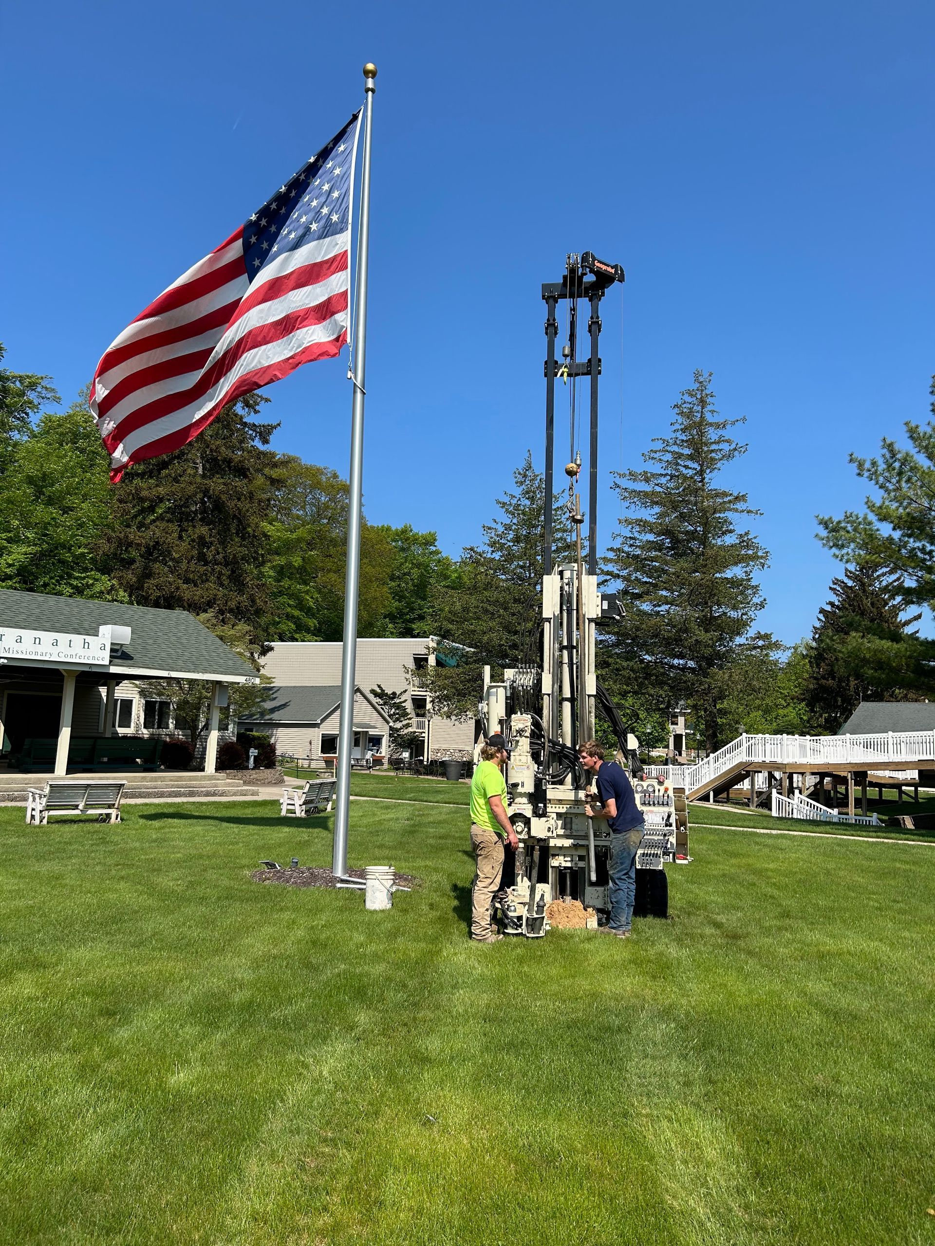 People gathered on a lawn near a U.S. flag and a tall pole under a clear blue sky.