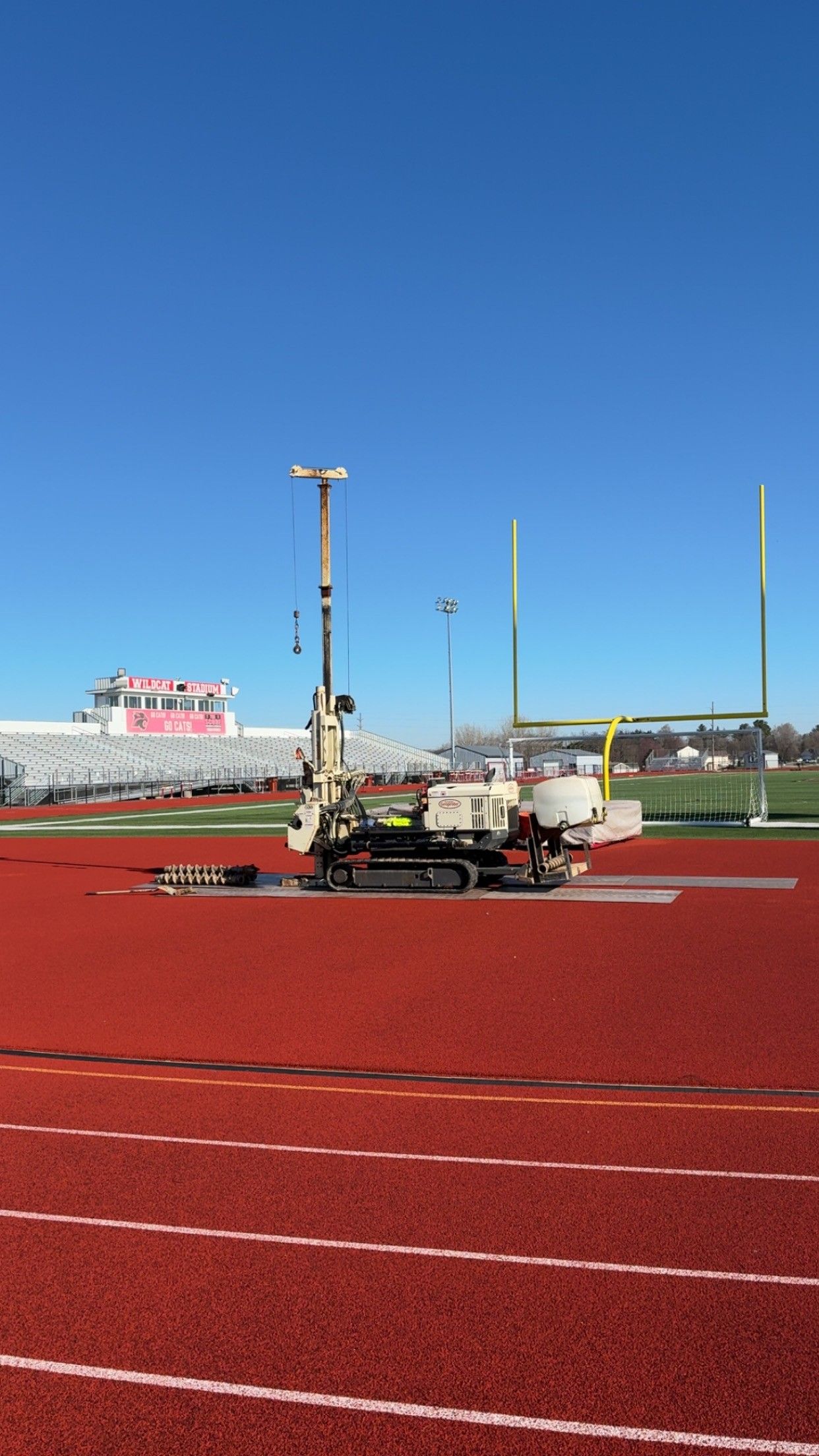 Construction machine on a red sports track under a clear blue sky.