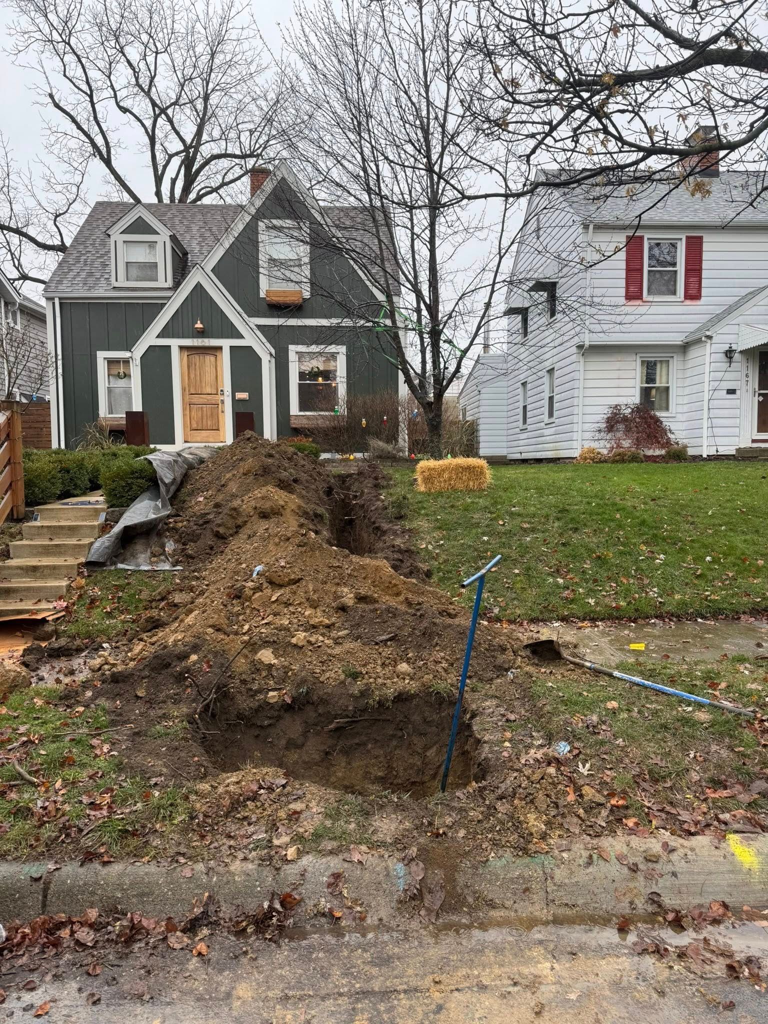 A large pile of dirt next to a house with steps; a trench is visible. Brown soil, green lawn.