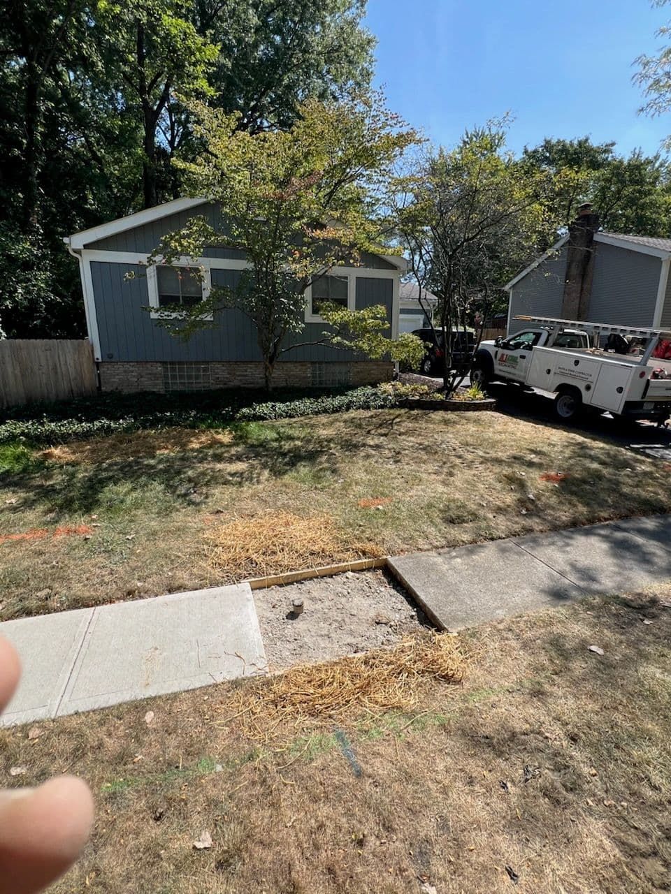 A house with a concrete sidewalk that has a missing section of concrete, with work trucks nearby.