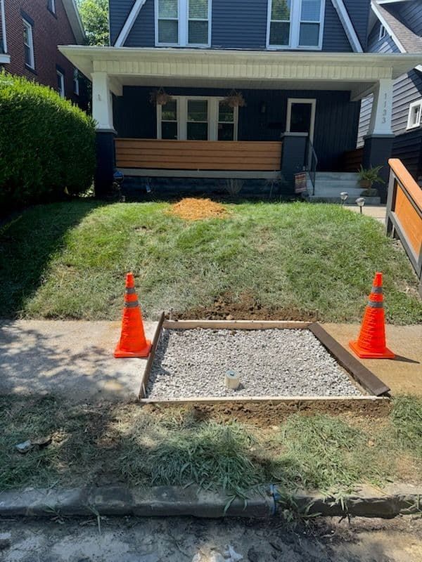 Sidewalk repair: square gravel patch bordered by wood, flanked by orange cones in front of a house.