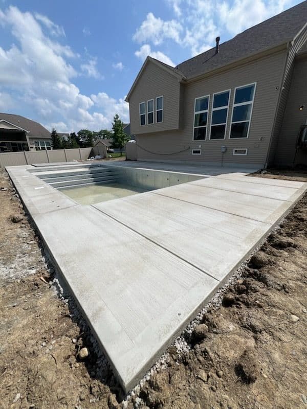 Concrete patio with a pool, next to a house, on a sunny day.