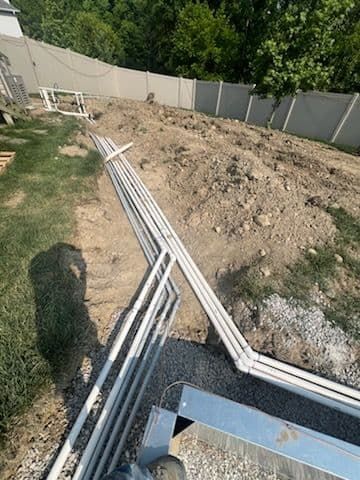 PVC pipes laid out on dirt, near a fence and green grass, preparing for construction.