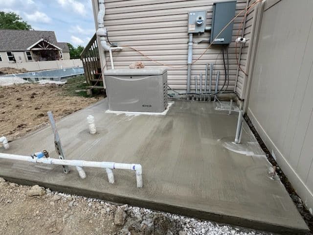 A concrete pad with a generator, pipes, and electrical box installed next to a house.