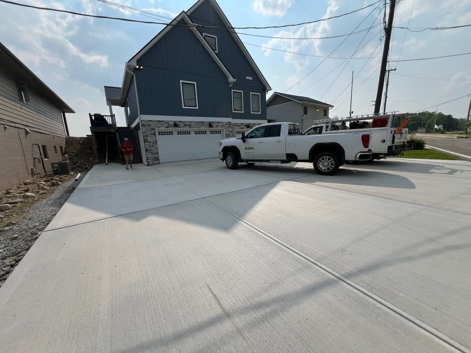 White truck parked in front of a blue house with a new concrete driveway on a sunny day.
