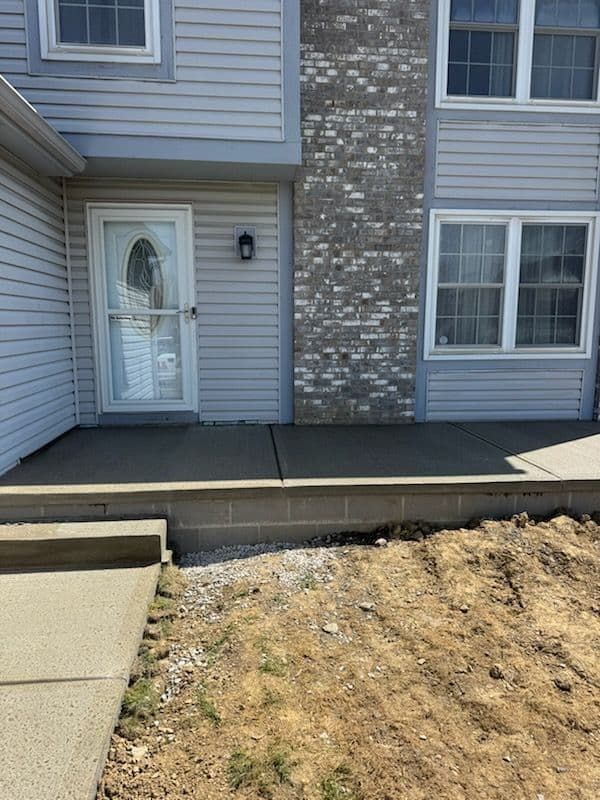 Exterior of a house with light blue siding, a concrete porch, and a brick chimney. Brown dirt in front.