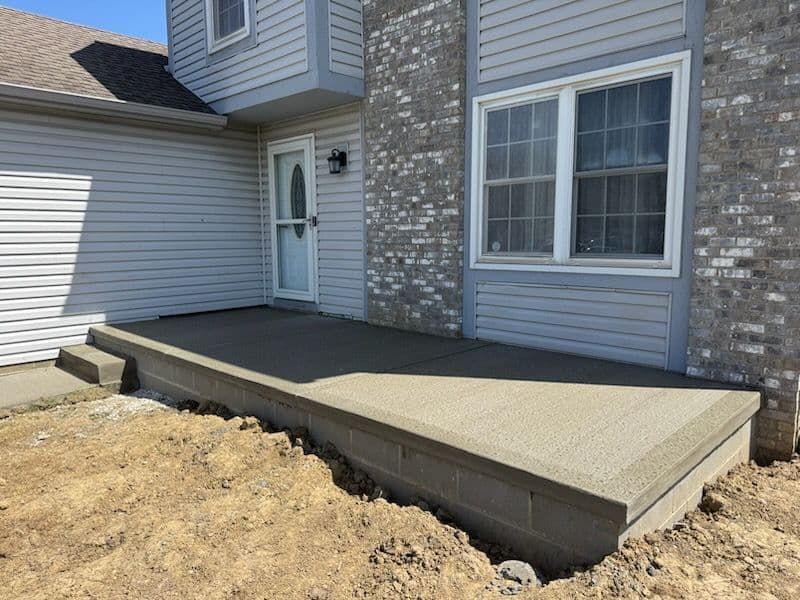 New concrete porch with steps, in front of a light-colored house with door and window.