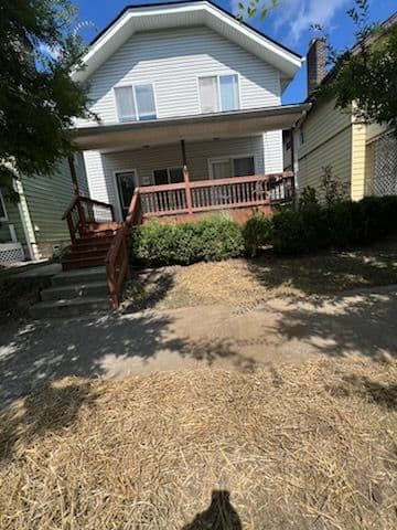 Two-story house with brown porch and stairs. Dry grass in the yard.