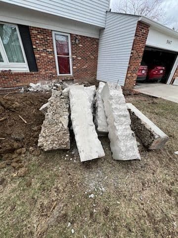 Pile of broken concrete blocks near a house, likely from a construction or demolition project.