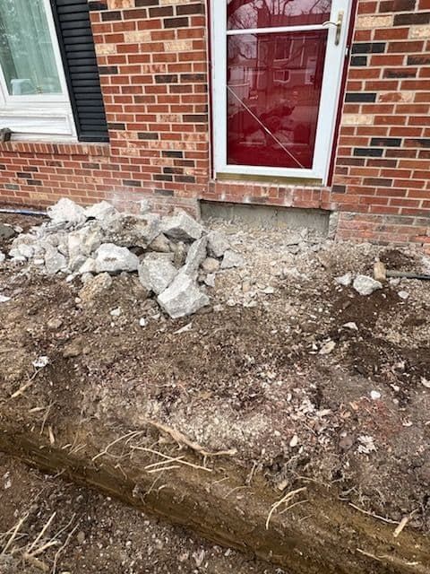 Pile of rubble and dug trench near the front door of a brick house during construction.