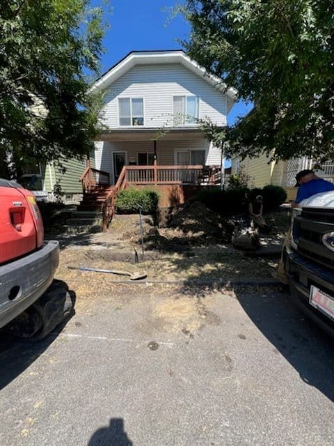 Two-story house with front yard under construction.  Red tractor on left, black SUV on right, blue sky.