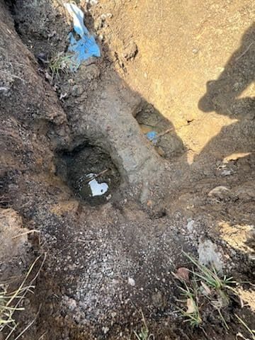 Hole dug in brown soil with a pipe running through, white paper inside.