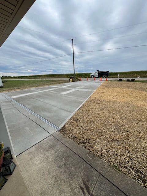New concrete driveway with grass on the right and a truck in the background under a cloudy sky.