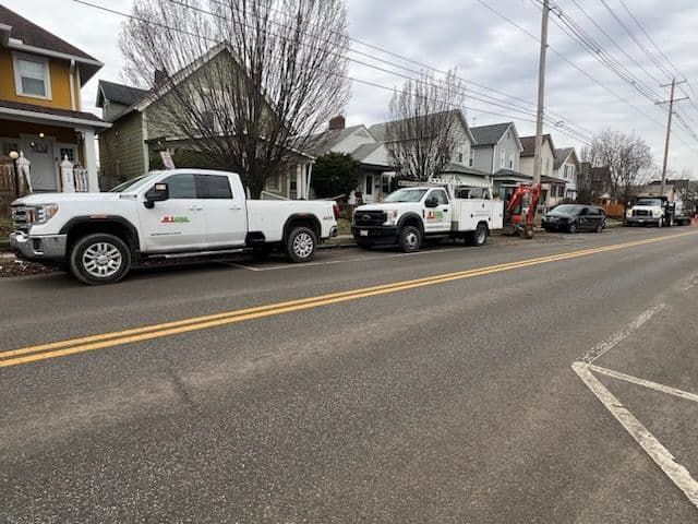 White trucks parked on a street in front of houses on a cloudy day.