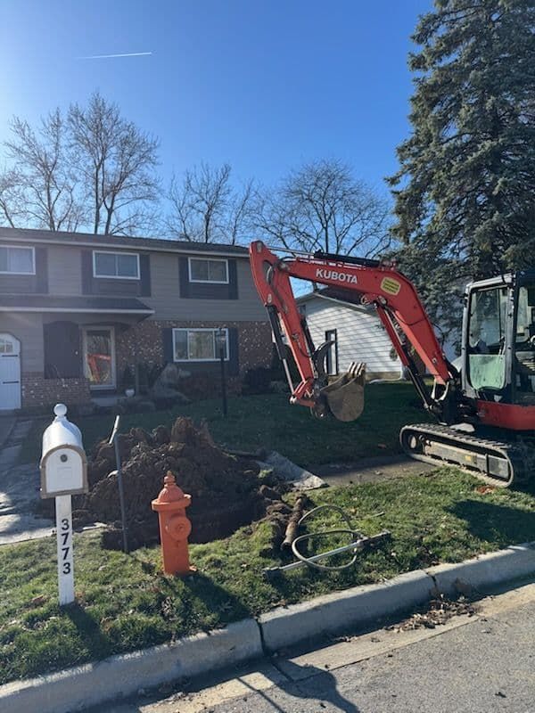 Excavator digging in a front yard near a house. The fire hydrant is orange. Sunny day.