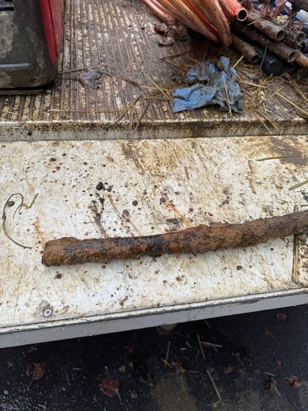 Rust-covered metal pipe on a dirty white surface with copper tubing in the background.