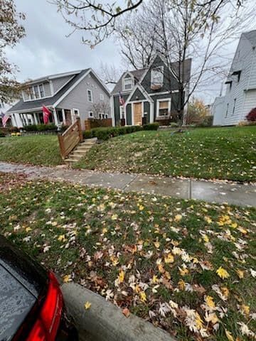 Suburban houses on a cloudy day, fallen leaves on the grass. Gray siding, wooden steps, flags.