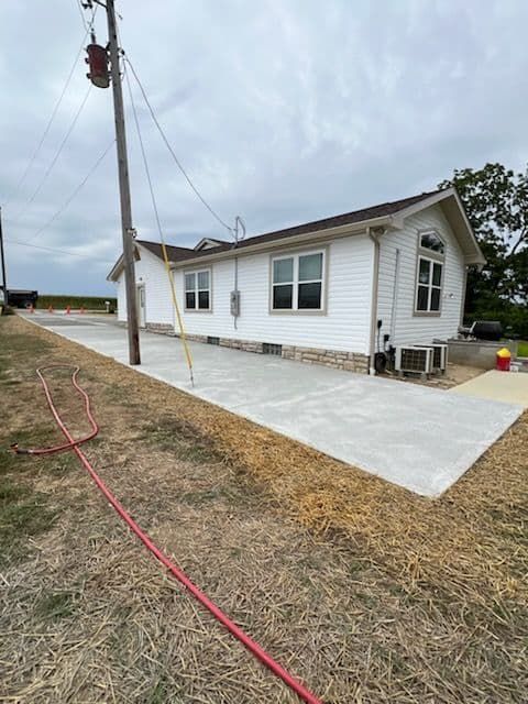 White house with brown roof and concrete driveway in rural setting.