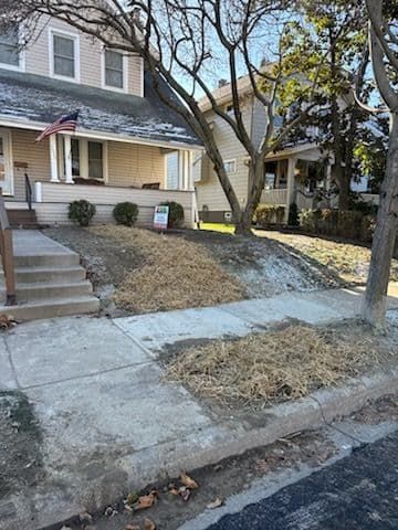 A two-story house with a yard covered in dry mulch and a sidewalk.