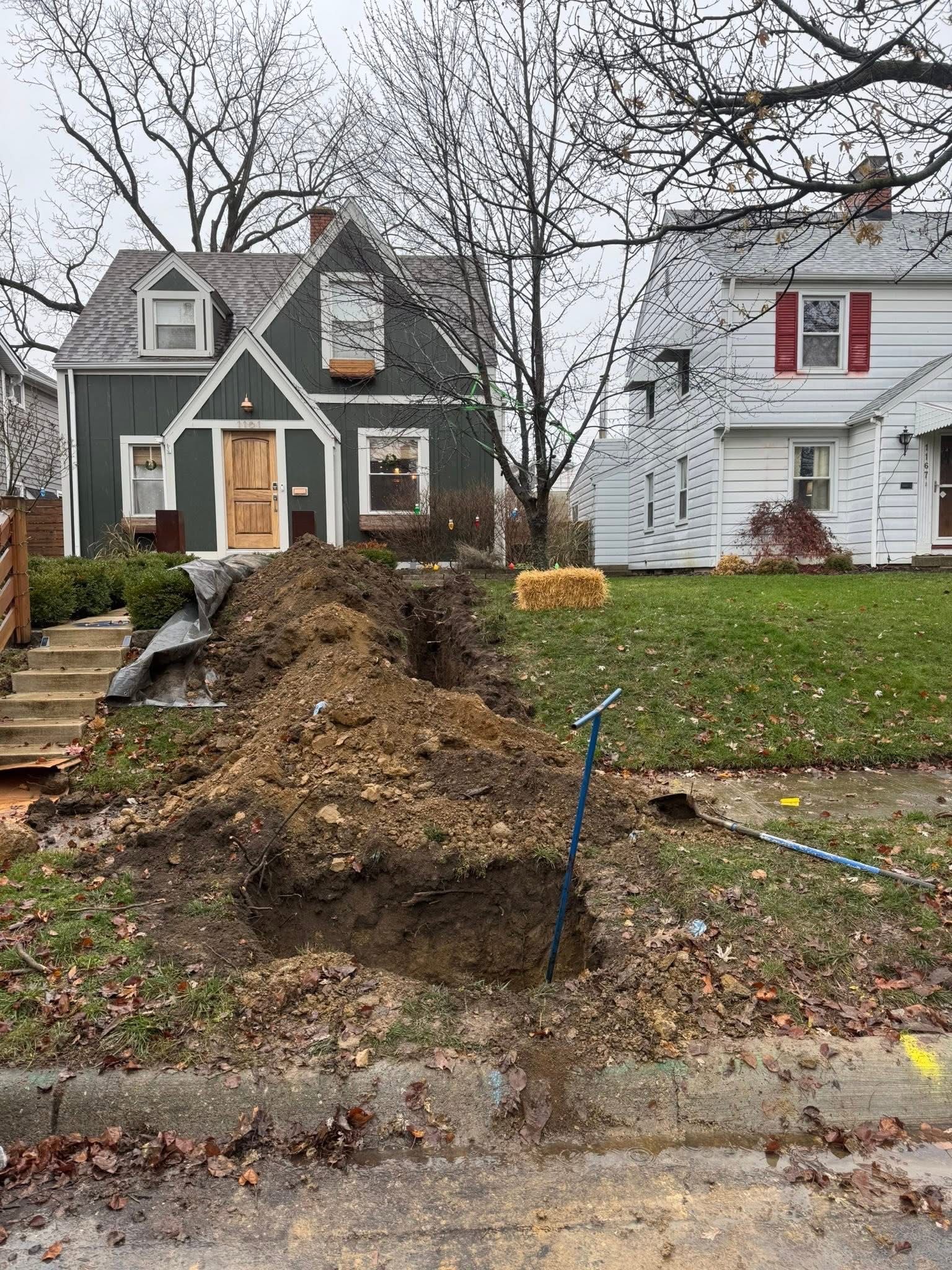 Dirt pile in front yard with a trench, two houses in background.