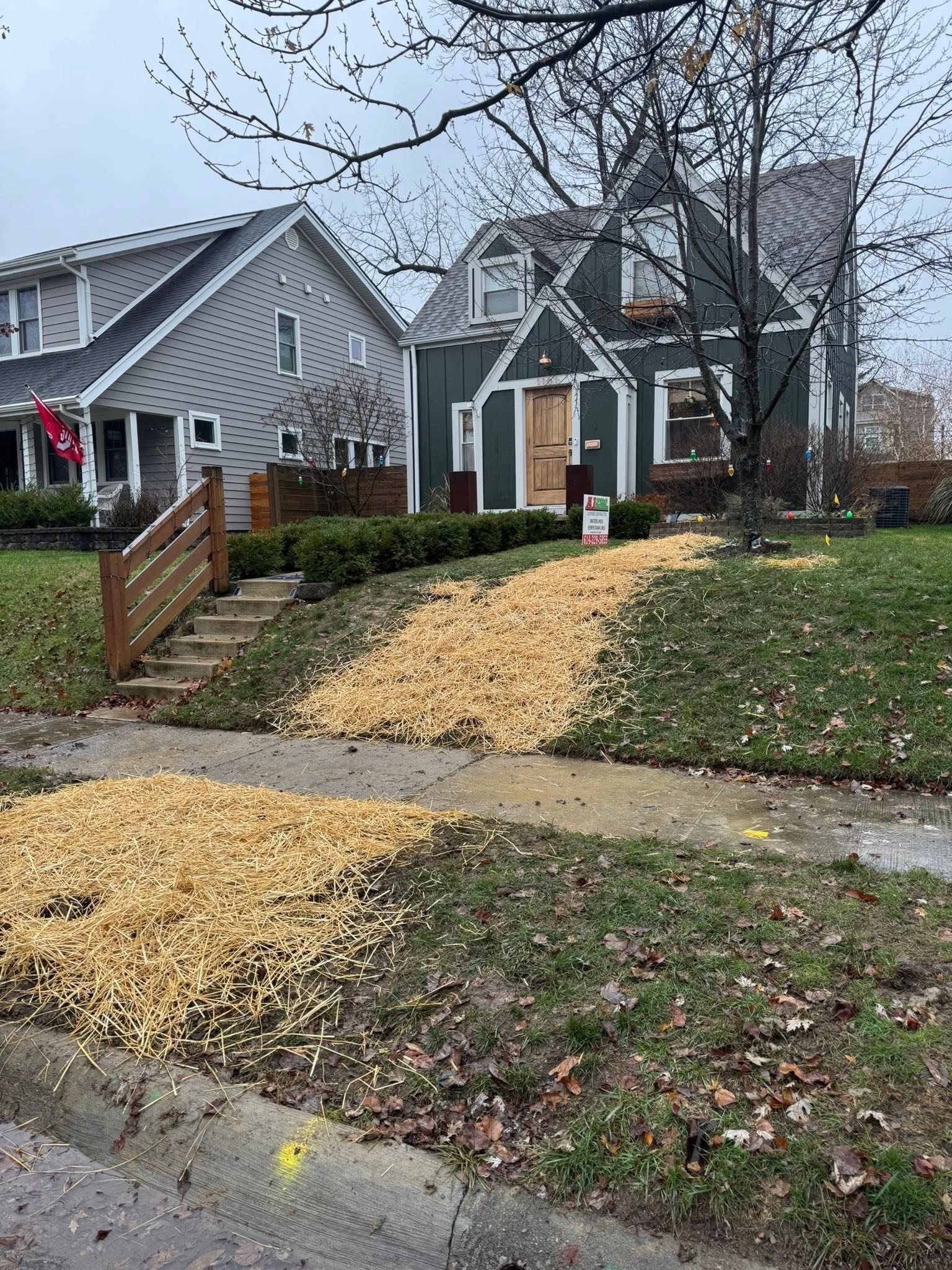 A house with a pile of wood chips on the lawn, partially blocking the sidewalk and driveway.
