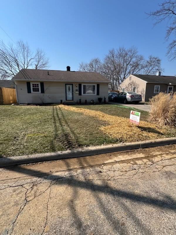 A ranch-style home with a lawn, tire tracks, and a for sale sign.