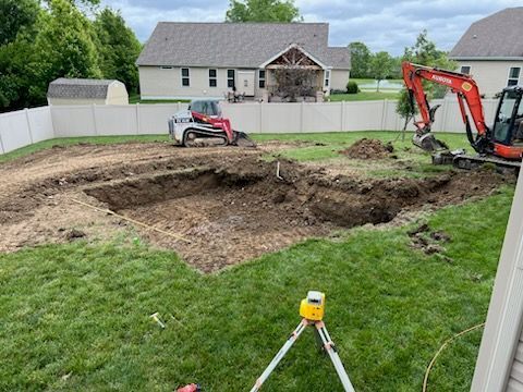 Backyard excavation for a pool. An excavator and skid steer, with dirt piled around the hole.