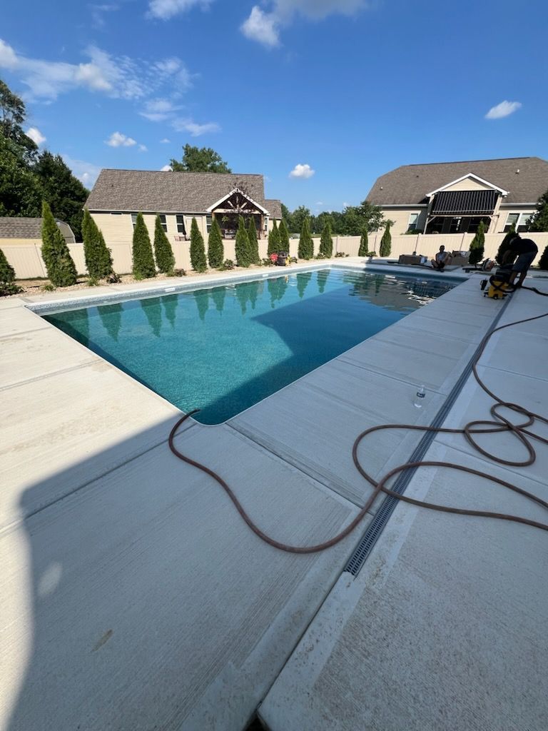 A rectangular pool with turquoise water, surrounded by concrete and homes under a blue sky.