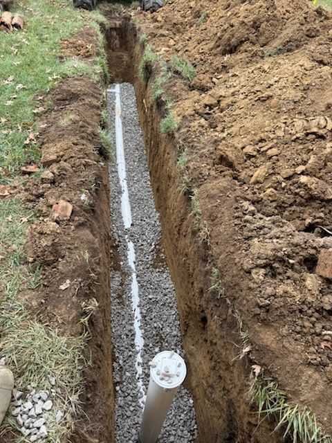 Trench with white pipe and gravel, likely for drainage, in a yard.