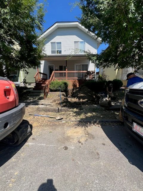 House with porch and yard under construction; excavator and vehicle in foreground.