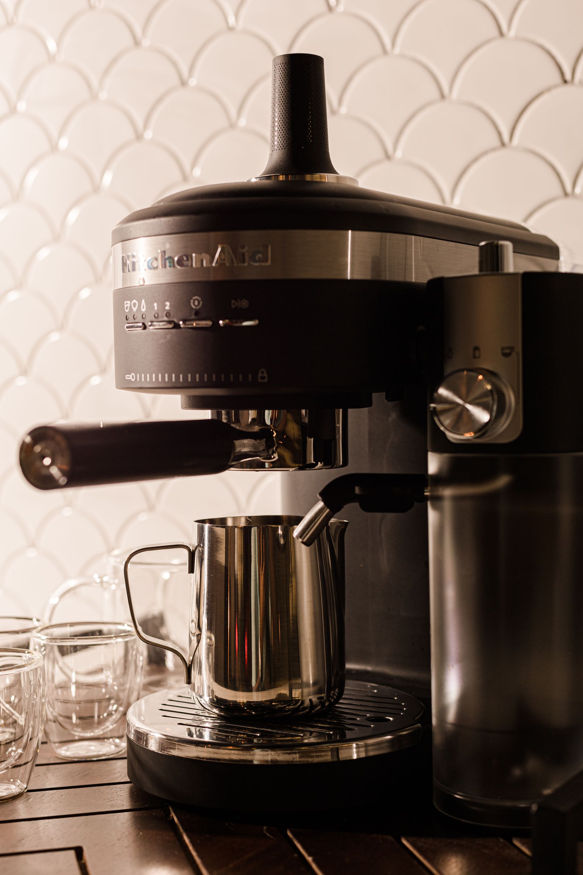 A black KitchenAid espresso machine on a counter with a metal steaming pitcher sitting on its drip tray.