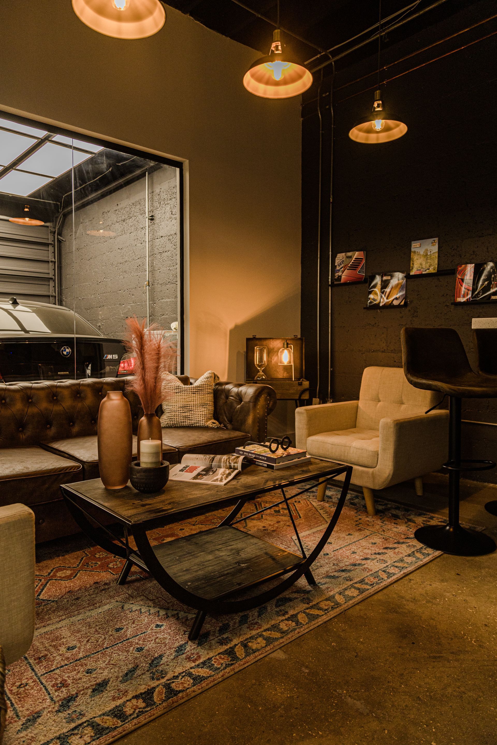 A cozy, dimly lit lounge featuring a brown leather sofa, an armchair, a patterned rug, and warm pendant lighting.